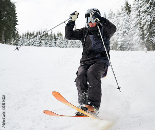 Man skier in black ski suit and goggles skiing downhill trough deep powder snow. Young man freerider in helmet using ski poles and gliding on snow at ski resort. Concept of skiing and active leisure. photo