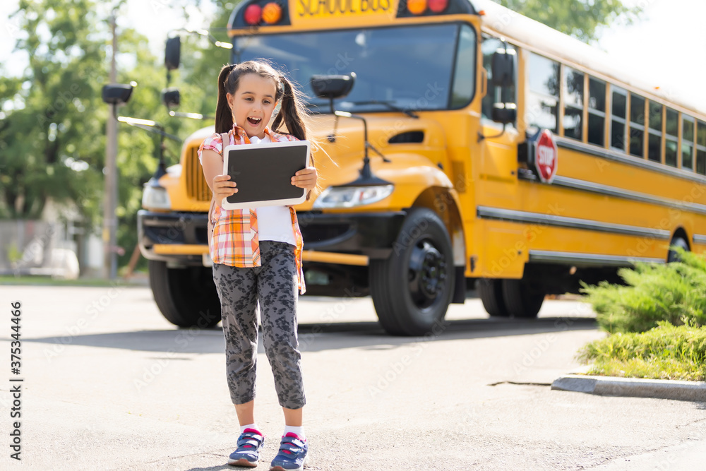 Little girl standing by a big school bus door with her backpack. Stock