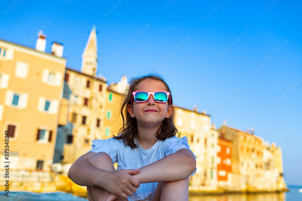 Funny little girl in sunglasses on sunny summer day. Rovinj town in background. Summer vacation at sea.