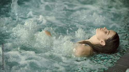 Young woman relaxing in pool at luxury spa. Beautiful girl bathing at jacuzzi