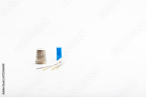 Minimalist detail of a silver metal thimble and needles of different sizes  used for sewing on a white background.