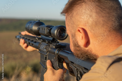 A hunter with a weapon on the hunt against the backdrop of a beautiful summer landscape. Shooter sighting in the target. The Bearded man is on the hunt. Soft focus