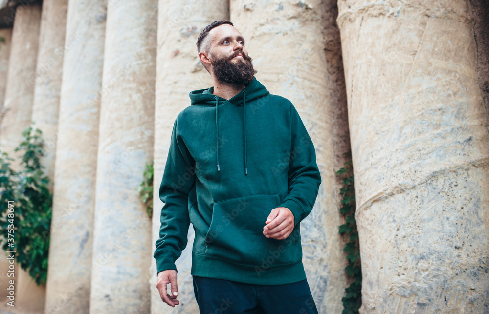 City portrait of handsome hipster guy with beard wearing green (watercolor) blank hoodie or sweatshirt with space for your logo or design. Mockup for print