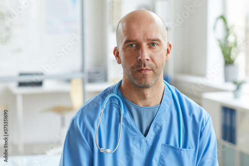 Medium close-up portrait shot of mature doctor wearing blue uniform looking at camera with serious facial expression