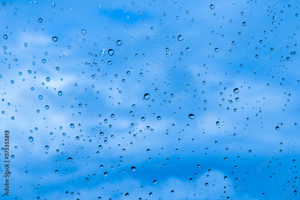 blue rain water drops on a window glass close up with sad clouds in background, drop macro texture ; bad weather backdrop blue rain water drops on a window glass close up with sad clouds in background, drop macro texture ; bad weather backdrop