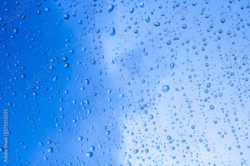 blue rain water drops on a window glass close up with sad clouds in background, drop macro texture ; bad weather backdrop