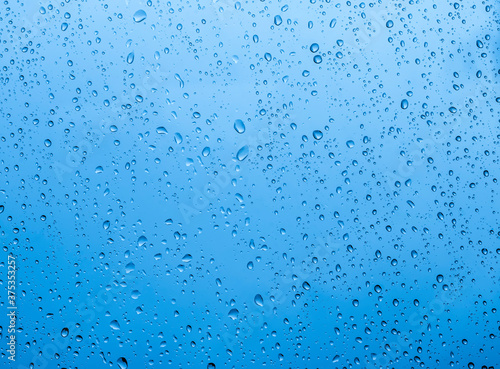 blue rain water drops on a window glass close up with sad clouds in background, drop macro texture ; bad weather backdrop
