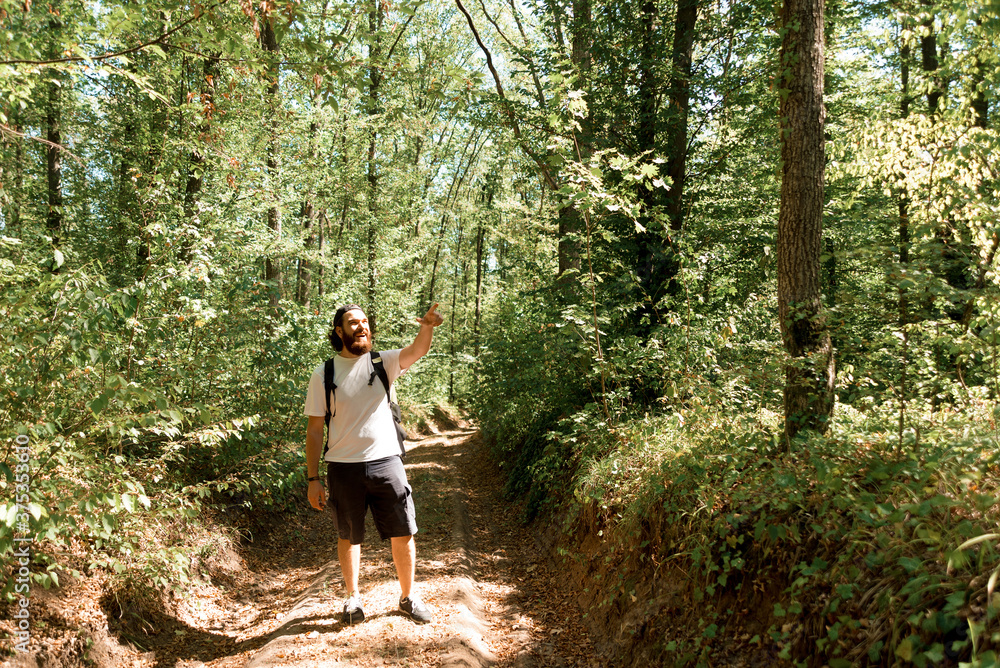 Photo of young traveler standing in middle of forest and pointin