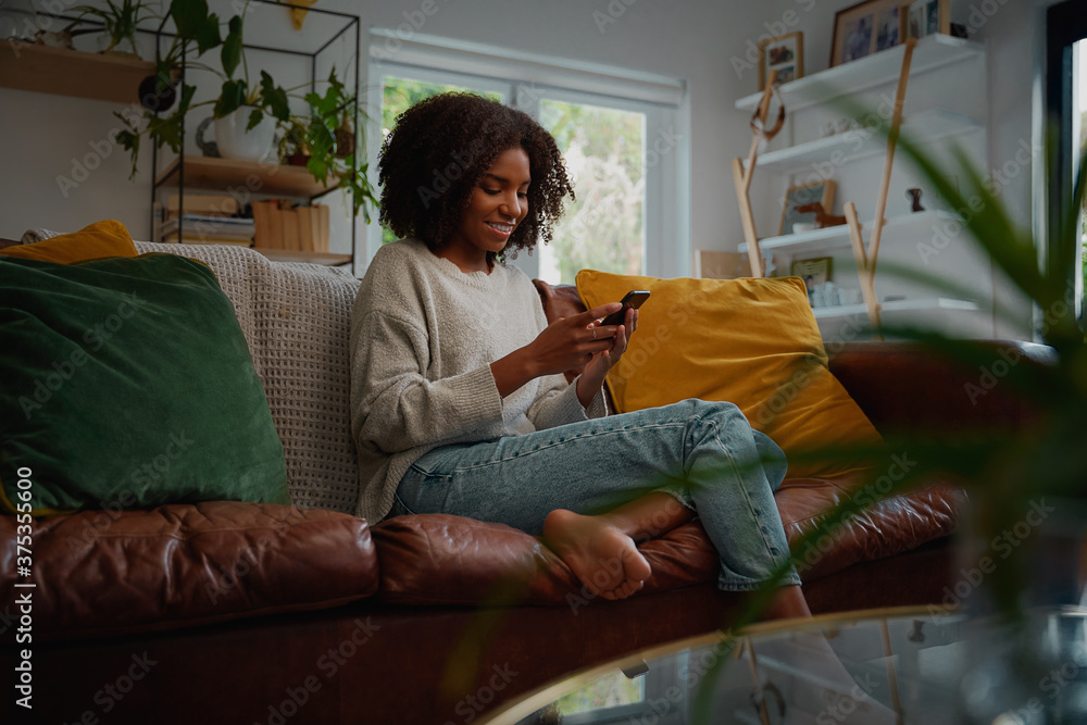 © StratfordProductions - Happy young african woman using mobile phone while sitting a couch at home © StratfordProductions - Happy young african woman using mobile phone while sitting a couch at home