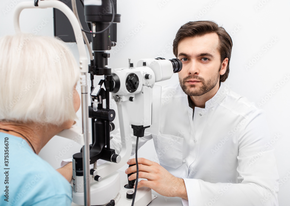 Optometrist doctor using a binocular slit-lamp examines the eye of an elderly woman patient. Aged people must be tested by an ophthalmologist Optometrist doctor using a binocular slit-lamp examines the eye of an elderly woman patient. Aged people must be tested by an ophthalmologist