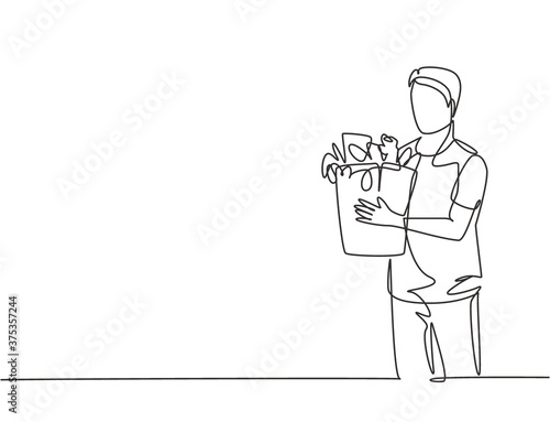 Single continuous line drawing young happy attractive man holding groceries bag full of daily needs. Buying organic product at grocery store concept. One line draw vector graphic design illustration