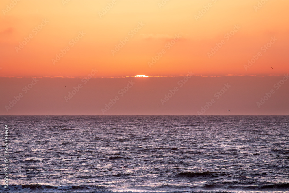 Fototapeta premium Sun disappearing behind clouds at sunset on the coast of Holland