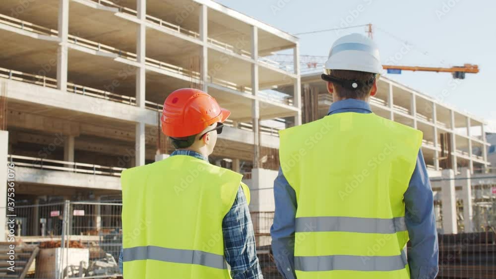 Professional builders standing in front of construction site. Office building and crane background. Professional builders standing in front of construction site. Office building and crane background.