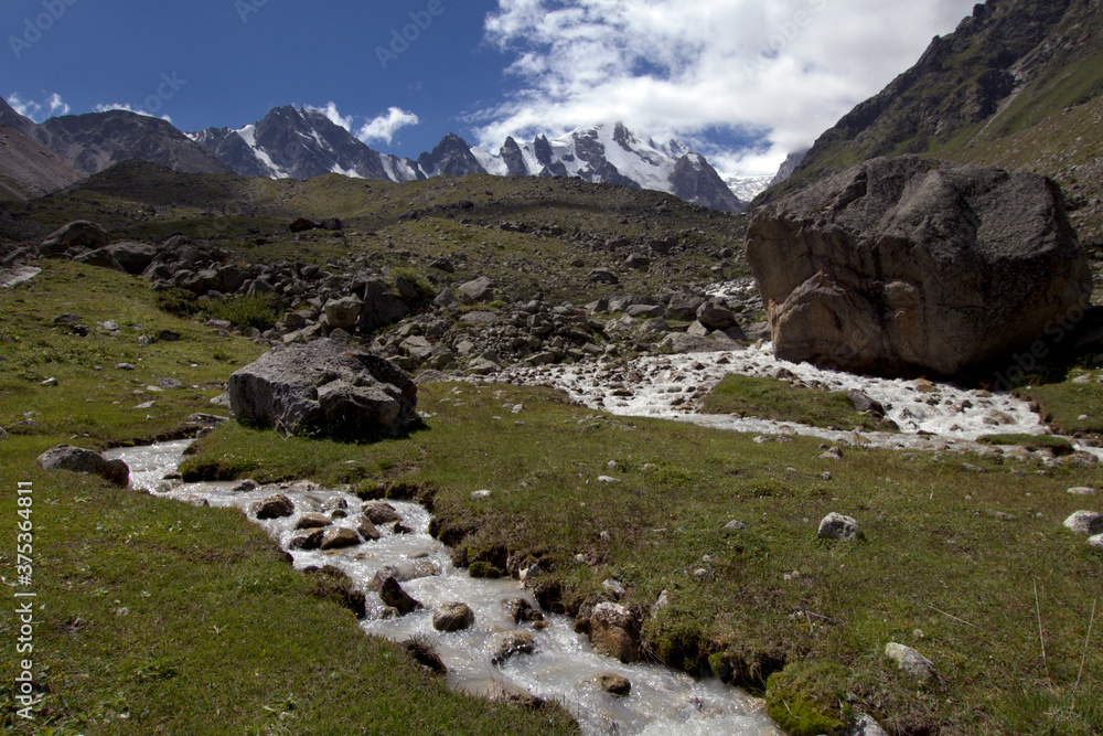 Snow-capped mountain peaks and mountain stream. Snow-capped mountain peaks and mountain stream in the foreground on a sunny summer day.