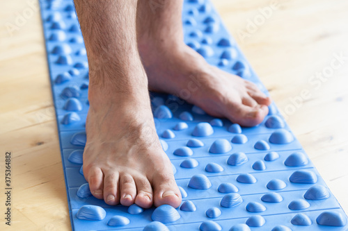 man doing flatfoot correction gymnastic exercise walking on massage mat at home
