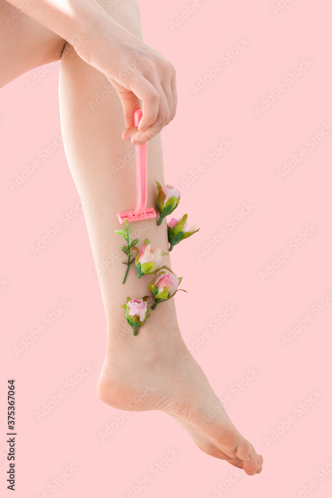 Woman's thin unshaven leg with pink flowers on a pink background. Female shaves her leg with a pink razor. Feminism