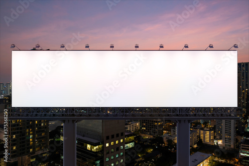 Blank white road billboard with Bangkok cityscape background at night time. Street advertising poster, mock up, 3D rendering. Front view. The concept of marketing communication to promote idea.
