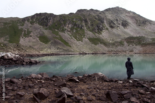 A tourist on the shore of a high-mountainous lake with rocky shores and emerald water. Alpine lake Giybashkel (3240 meters above sea level), Caucasus. 