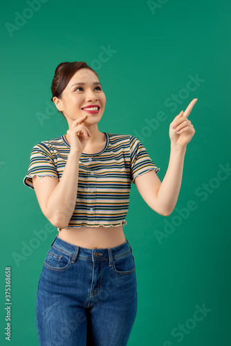 Smiling happy young Asian woman pointing her hand over green background.