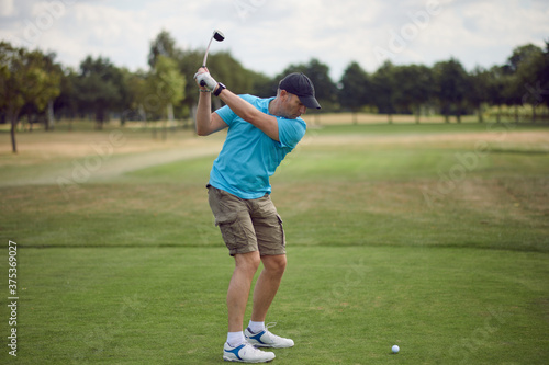 Man playing golf swinging at the ball as he plays his shot using a driver viewed from behind looking down the fairway in a healthy active lifestyle concept