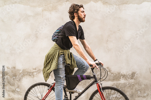 Young bearded guy riding his bike against a white wall in the city