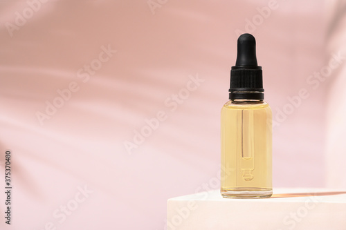 Beauty mineral oil glass bottle with dropper for skin, hair. Product package serum on pink background and white stand. Woman cosmetics skincare cream on podium, backdrop and palm shadow. Copy space