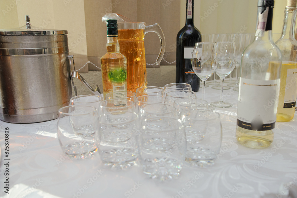 Bottle of cold vodka and wine bottle in bucket with ice and orange juice in jug on table, copy space. Alcohol bottles in ice bucket in restaurant. Wedding party. Bottle of cold vodka and wine bottle in bucket with ice and orange juice in jug on table, copy space. Alcohol bottles in ice bucket in restaurant. Wedding party.