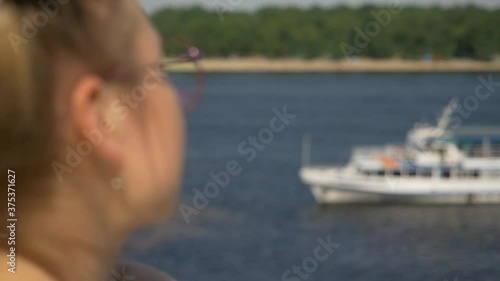 Beautiful attractive cute girl in a good mood at the observation deck enjoys a view of the city, river and ships. Close-up.