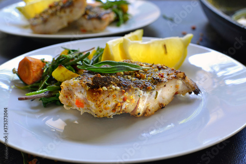 Grilled fish with lemon, herbs and rosemary. Fried fish fillets in a white plate. Beautiful presentation of food. Rucolla salad and carrots. Close-up.