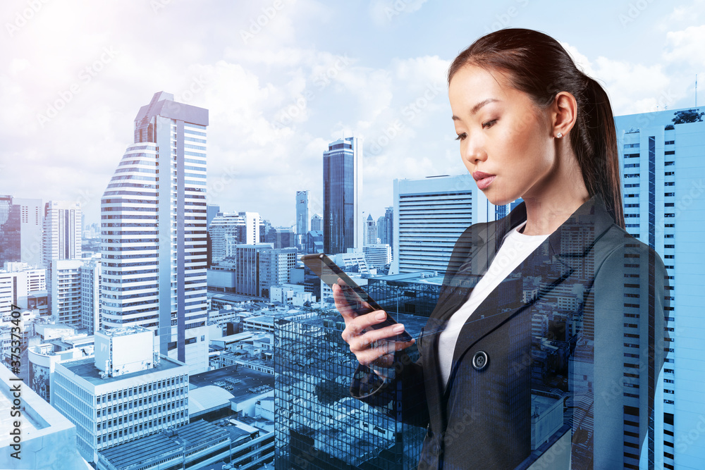 Prosperous astonishing young Asian business woman in suit texting phone the details of corporate meeting. Bangkok cityscape. The concept of business communication. Double exposure. Prosperous astonishing young Asian business woman in suit texting phone the details of corporate meeting. Bangkok cityscape. The concept of business communication. Double exposure.