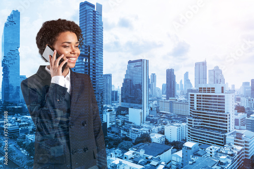 Successful smiling black African American business woman in suit pensively talking phone, Bangkok cityscape. The concept of consultants as problem solvers. Double exposure.