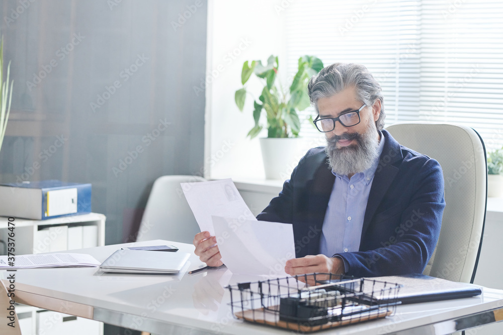 Portrait of modern mature HR manager sitting alone in office room reading CV papers before interviewing applicants Portrait of modern mature HR manager sitting alone in office room reading CV papers before interviewing applicants