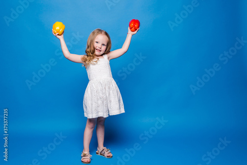 Beautiful little girl holds in bell pepper on blue background