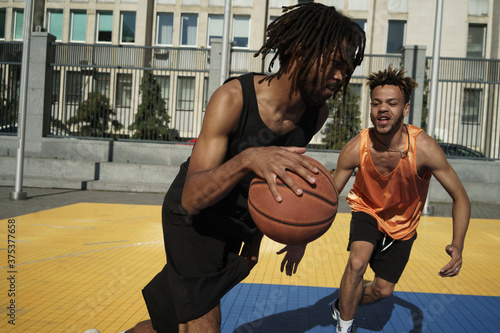 Image of african american guys playing basketball on city sports ground