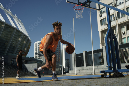 Image of african american guy playing basketball on city sports ground