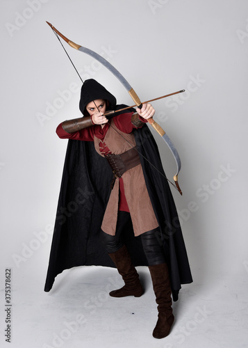 Fotografia Full length portrait of girl with red hair wearing medieval archer costume with black cloak