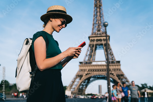 Caucasian woman browsing wireless network during time for romantic French walk in Paris, carefree female tourist enjoying smartphone communication standing at street with Eiffel Tower on background © BullRun
