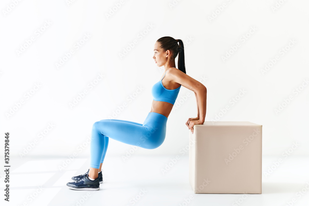 Sporty woman practicing squat exercises with big cube over white background. Sporty woman practicing squat exercises with big cube over white background.