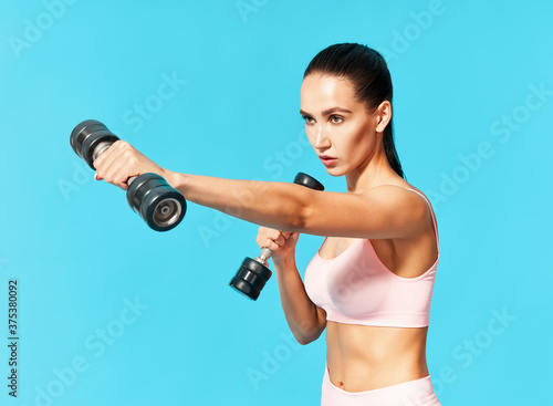 Young sporty woman in sportswear doing exercise with dumbbells on blue background