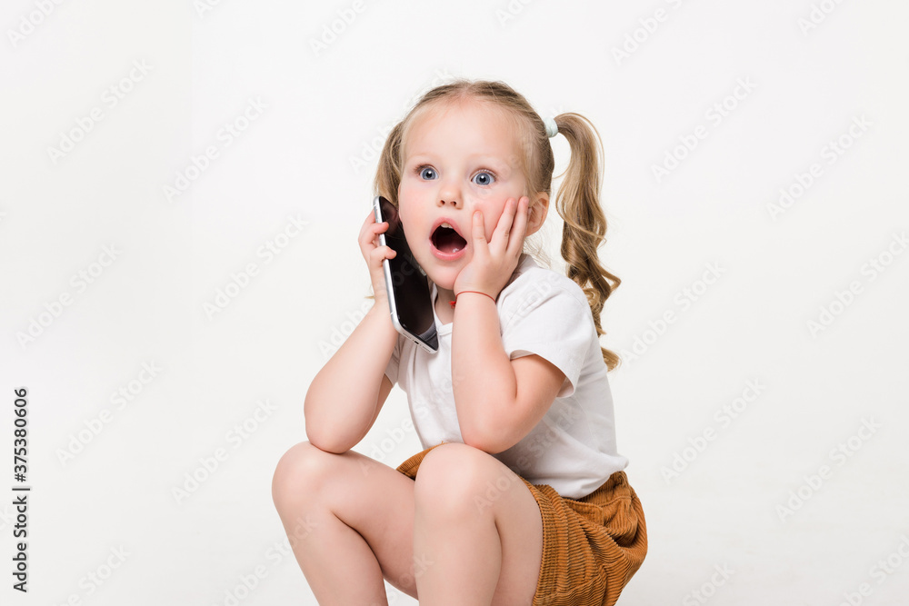 Portrait of shocked little girl talk phone sitting on a stack of books over white background. Portrait of shocked little girl talk phone sitting on a stack of books over white background.