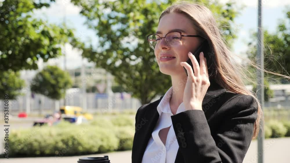 Beautiful businesswoman wearing white shirt and glasses and using mobile phone while walking at break in the city, outside, slow motion. Beautiful businesswoman wearing white shirt and glasses and using mobile phone while walking at break in the city, outside, slow motion.