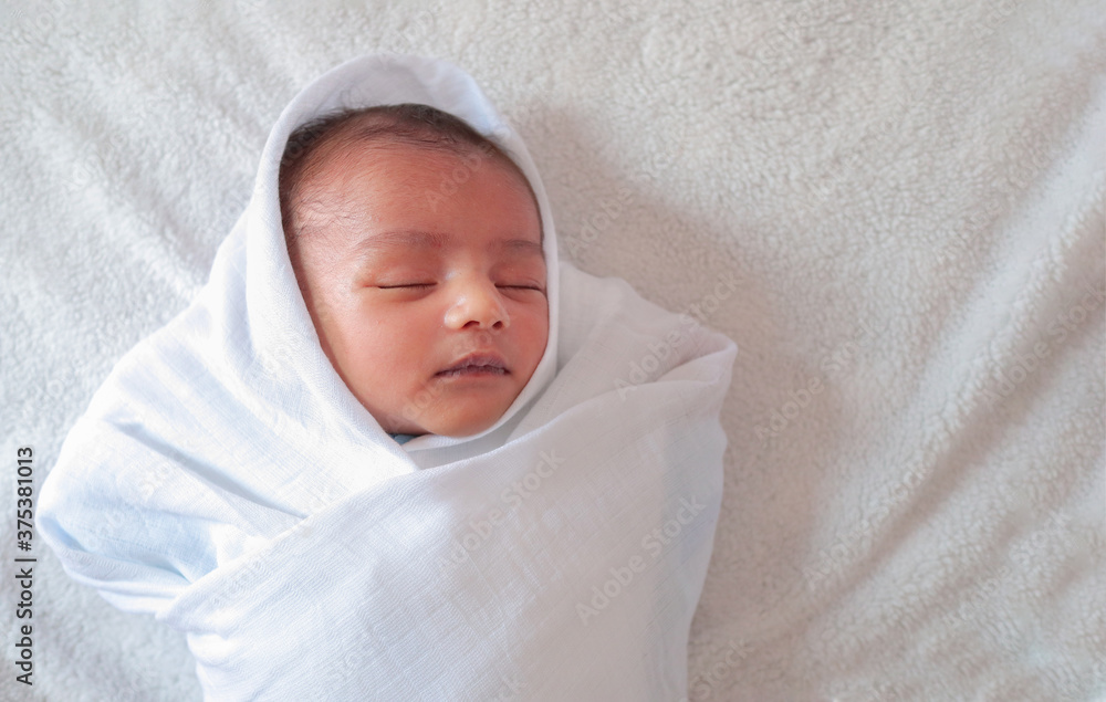 a one month old baby sleeping and swaddled in white cloth lying in
