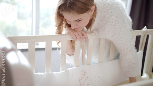 Canvas Print Happy mother near baby crib. Mom looking on sleeping child in cot