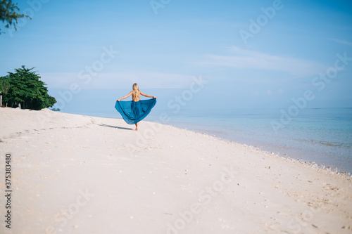 Woman walking on beach and holding hem of dress
