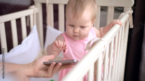 Cute baby in crib touch smartphone. Baby technology concept
