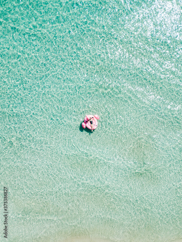 Aerial view of young sexy girl in black swimwear lie on inflatable pink flamingo in azure sea water, swim, sun bathe relax on beach Punta Prosciutto Italian Maldives Puglia Italy. Summer time vacation