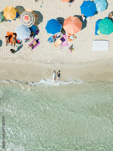 Aerial view of two young women in swimwear lie on sand beach Punta Prosciutto Puglia Italy. Italian Maldives. Summer vacation. People sun bathe swim lie under umbrellas relax. Sea waves hot sunny day