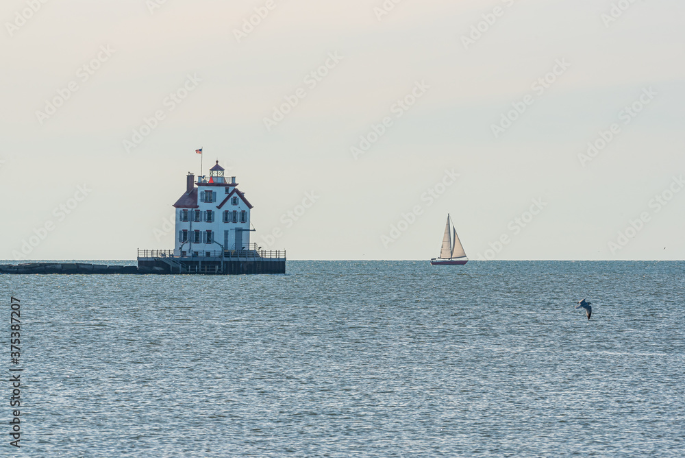 Sailboat sailing past lighthouse in calm water in summer