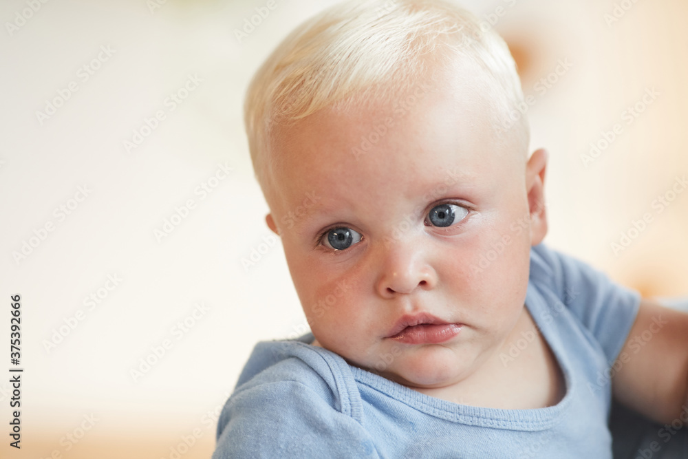 Horizontal close-up portrait shot of cute little baby boy with blond hair and blue eyes looking away, copy space