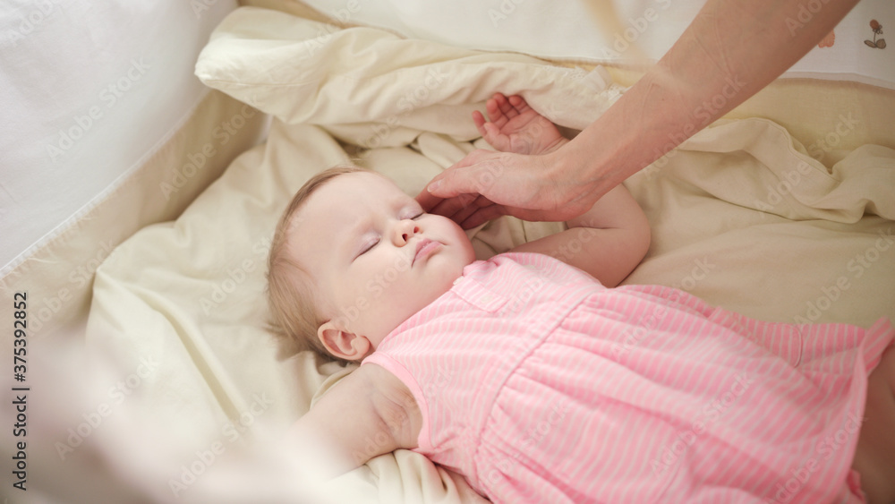 Beautiful baby sleeping in crib. Mother hands stroking sleeping kid Beautiful baby sleeping in crib. Mother hands stroking sleeping kid